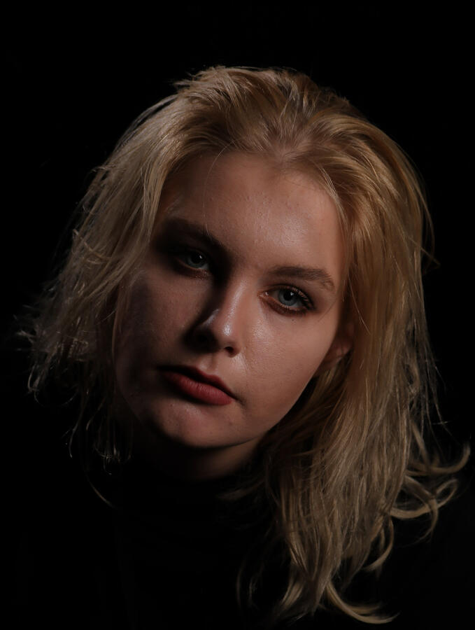 Eine Fotografie einer jungen Frau, man sieht ihr Gesicht und der Hintergrund ist schwarz