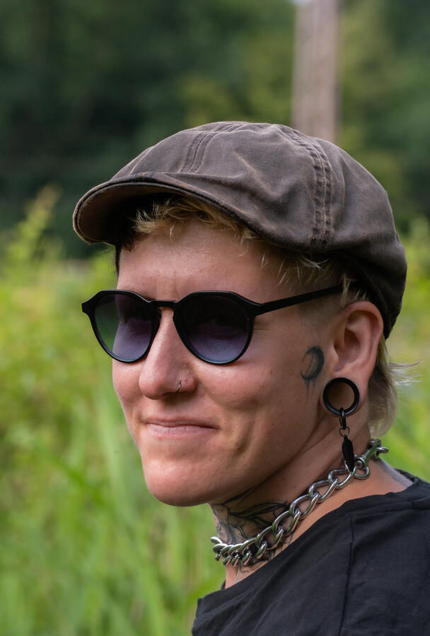 Das Gesicht einer Frau ist zu sehen, sie hat Tattoos und trägt eine Sonnebrille
