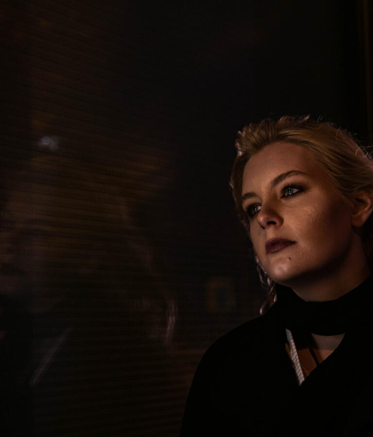 Portrait bei Nacht vor einer Scheibe, das Gesicht der Frau spiegelt sich in der Scheibe.